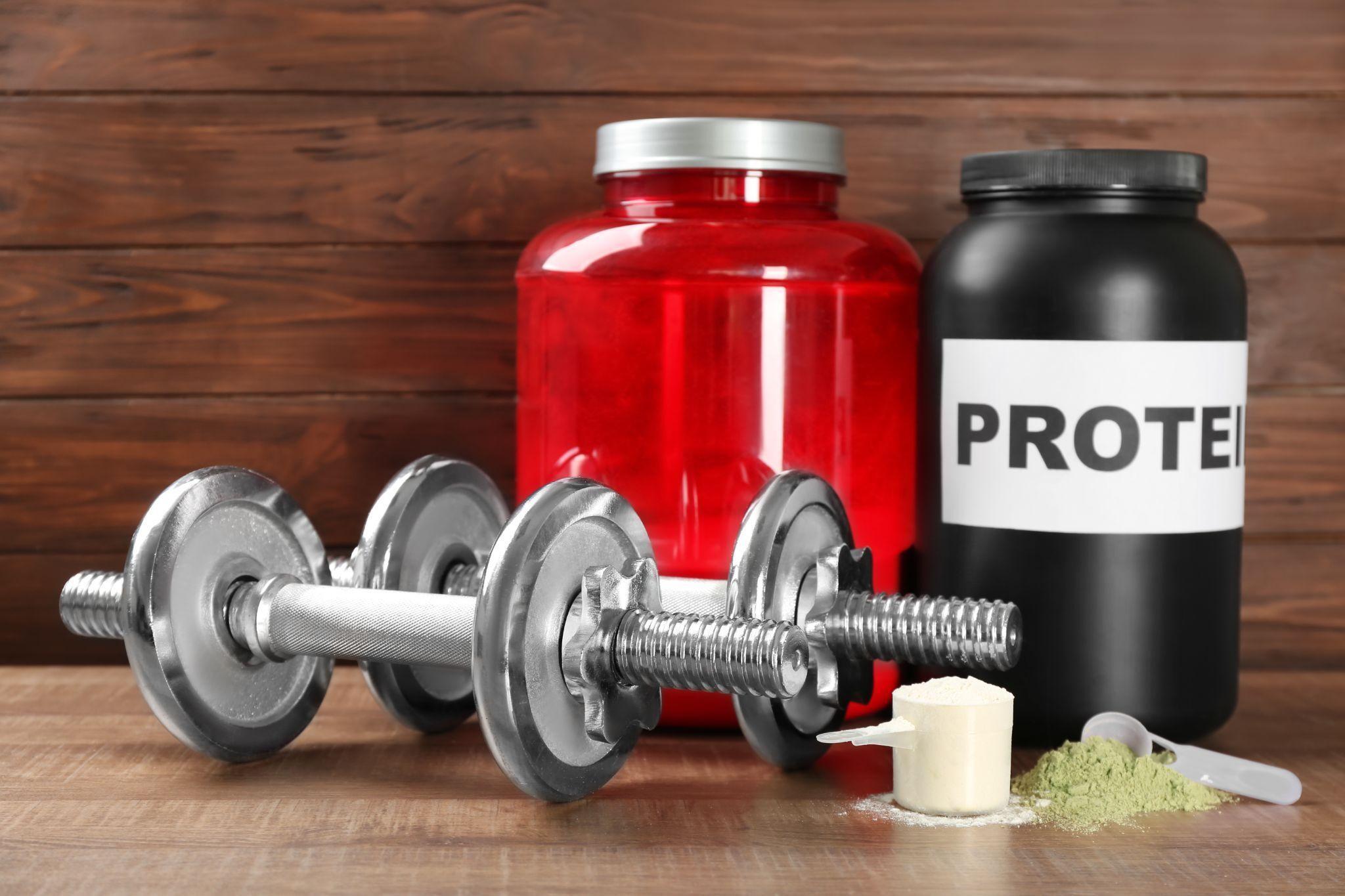 Composition with hemp and whey protein powder and dumbbells on wooden background